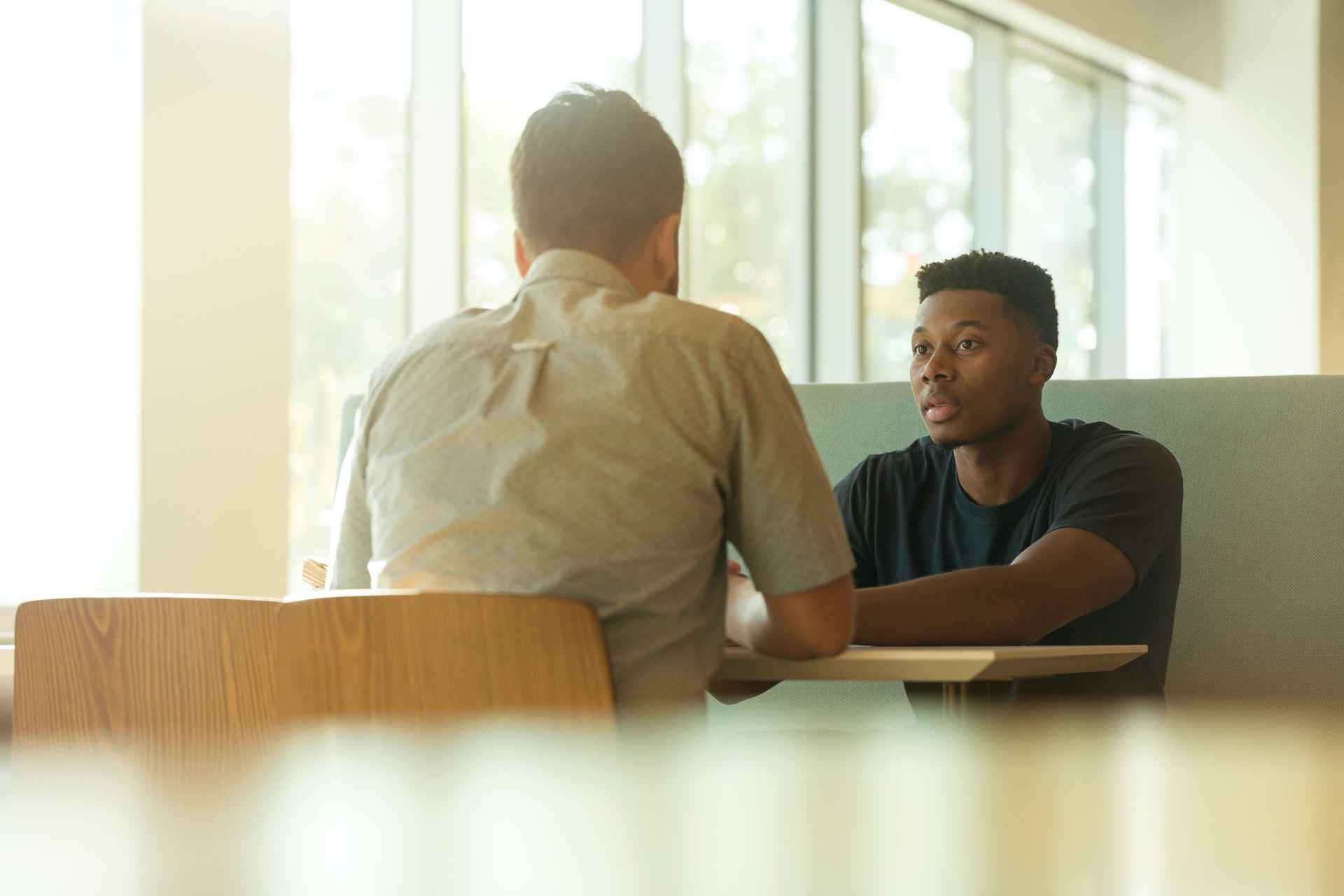 Two men sitting at a table facing each other, one providing feedback to the other