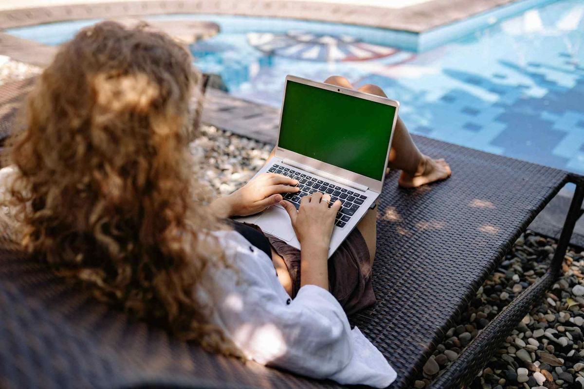 Woman sitting with laptop in front of a pool enjoying pool office as an employee appreciation idea