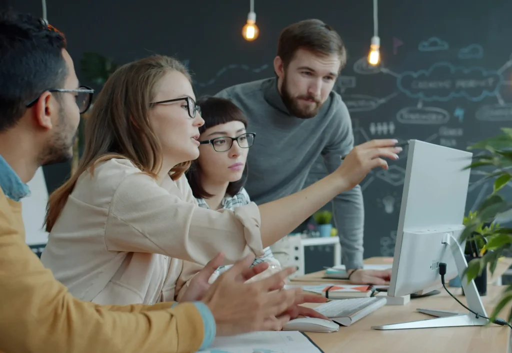 A diverse team of professionals collaborating at a desk, discussing ideas while looking at a computer screen — representing a scalable hiring process.