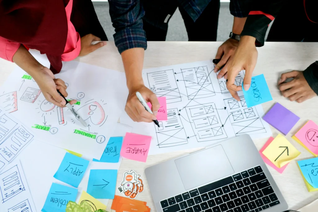 A team collaborating around diagrams and sticky notes, planning a step-by-step workflow to illustrate the marketing-style hiring funnel in SMB hiring trends.