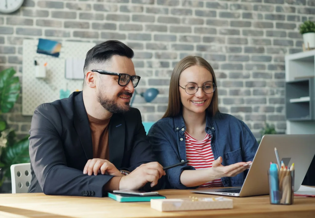 Two colleagues collaborating at a desk, reviewing content on a laptop and discussing results, illustrating AI job ad optimization and collaborative recruitment strategy.