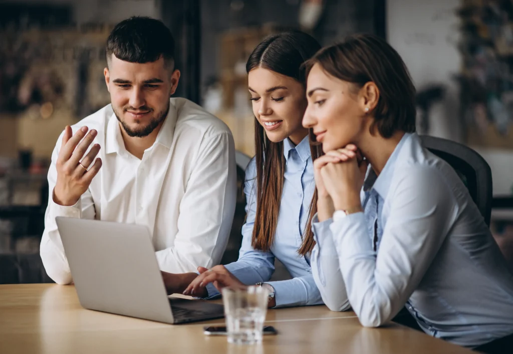 Recruitment team collaborating around a laptop during candidate management, reviewing applicant data and discussing hiring decisions.