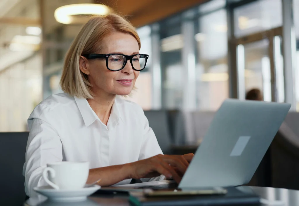 A small business owner in glasses working on a laptop in a modern office, managing the hiring process without an HR department.