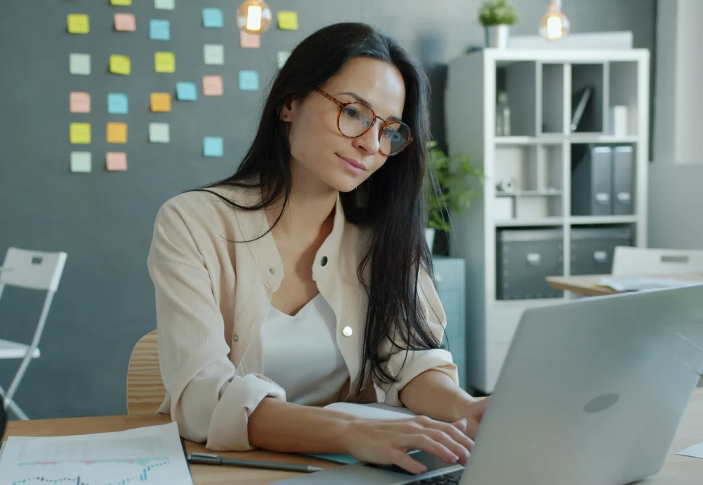 A focused hiring manager reviewing an interview scorecard on a laptop in a modern office with sticky notes on the wall.