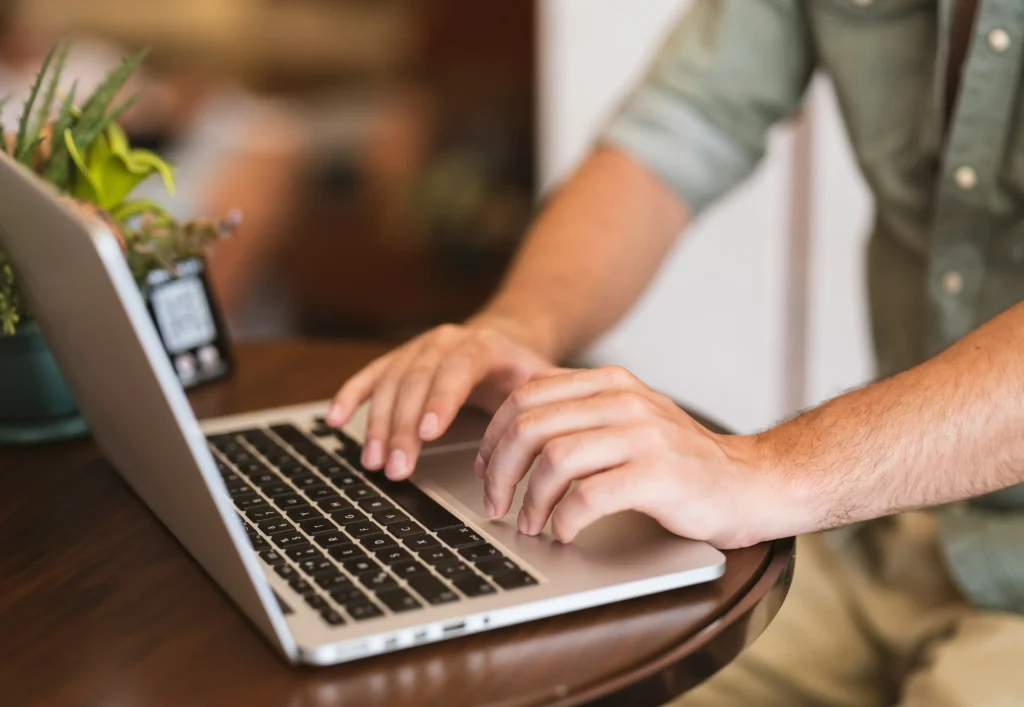 Close-up of a hiring manager typing structured interview questions on a laptop at a wooden desk.